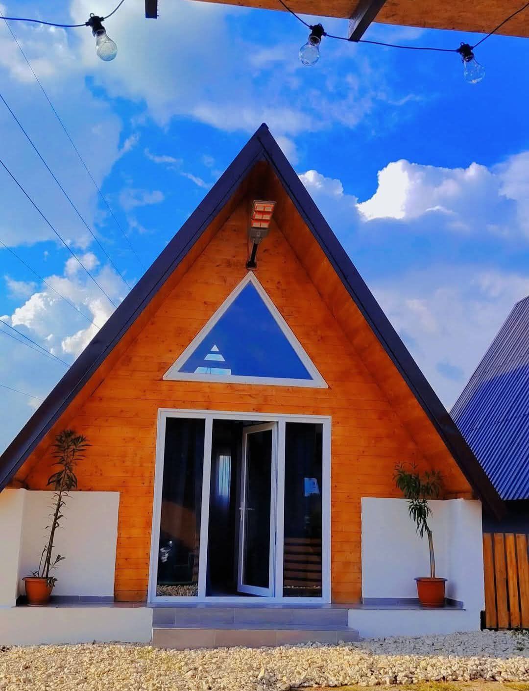 Fațada unei cabane A-Frame, cu ușă dublă din sticlă și cer albastru